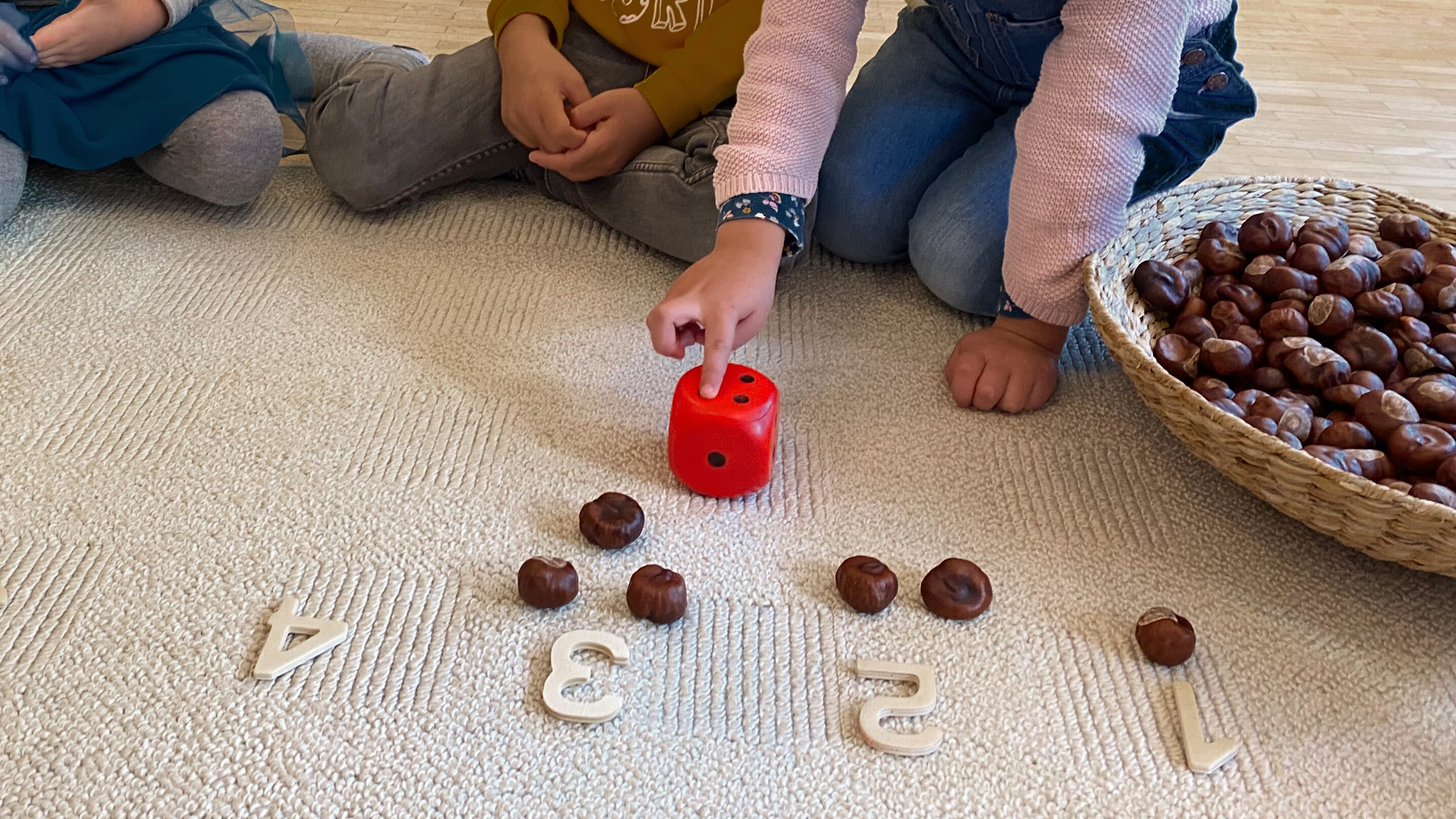 Kinder lernen spielend mit Würfel und Kastanien die Zahlen kennen