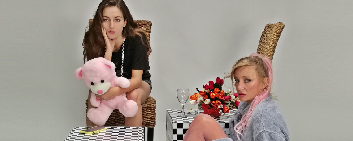 Die beiden Darstellerinnen sitzen in Bademantel mit Teddibär und leerem Glas zusammen