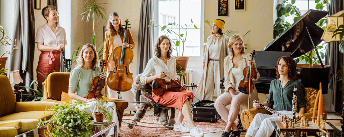 Die sieben Musikerinnen mit Instrumenten in einer gemütlichen Wohnung
