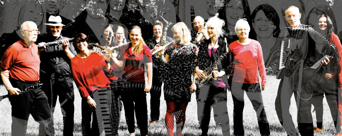 Die 13 Musiker:innen des Orchesters mit Instrumenten, in rot und schwarz gekleidet